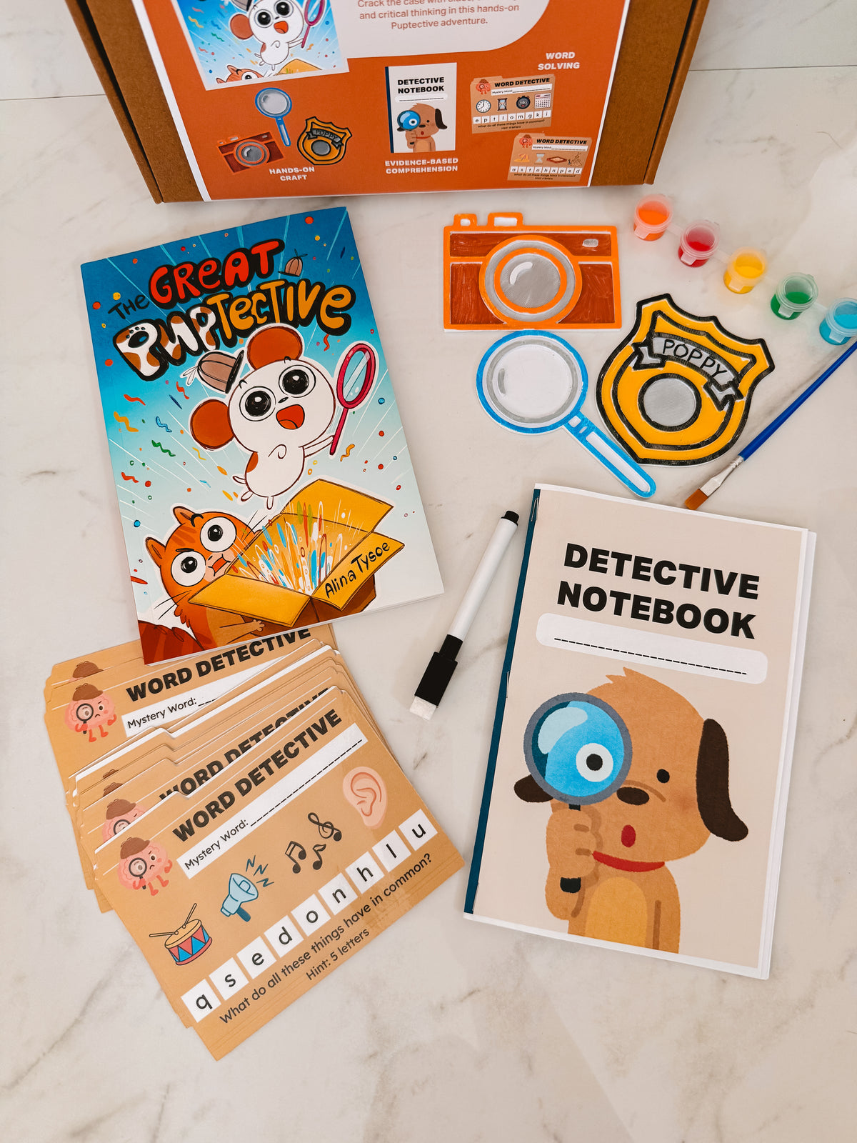 Children's detective-themed educational materials including a book, notebook, and cards on a light surface.