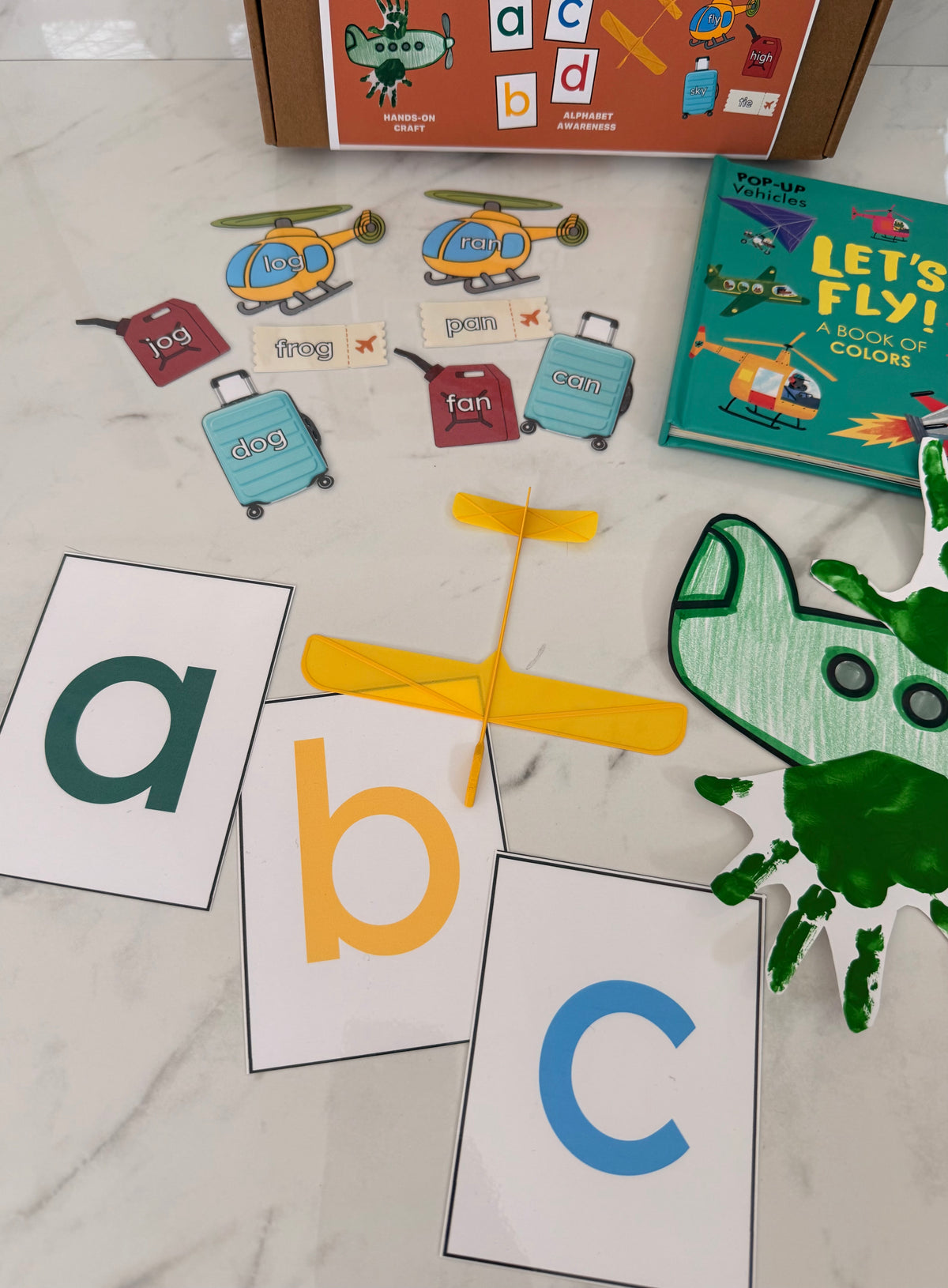 Educational children's items including alphabet cards, a book titled 'Let's Fly!', and toy letters on a marble surface.