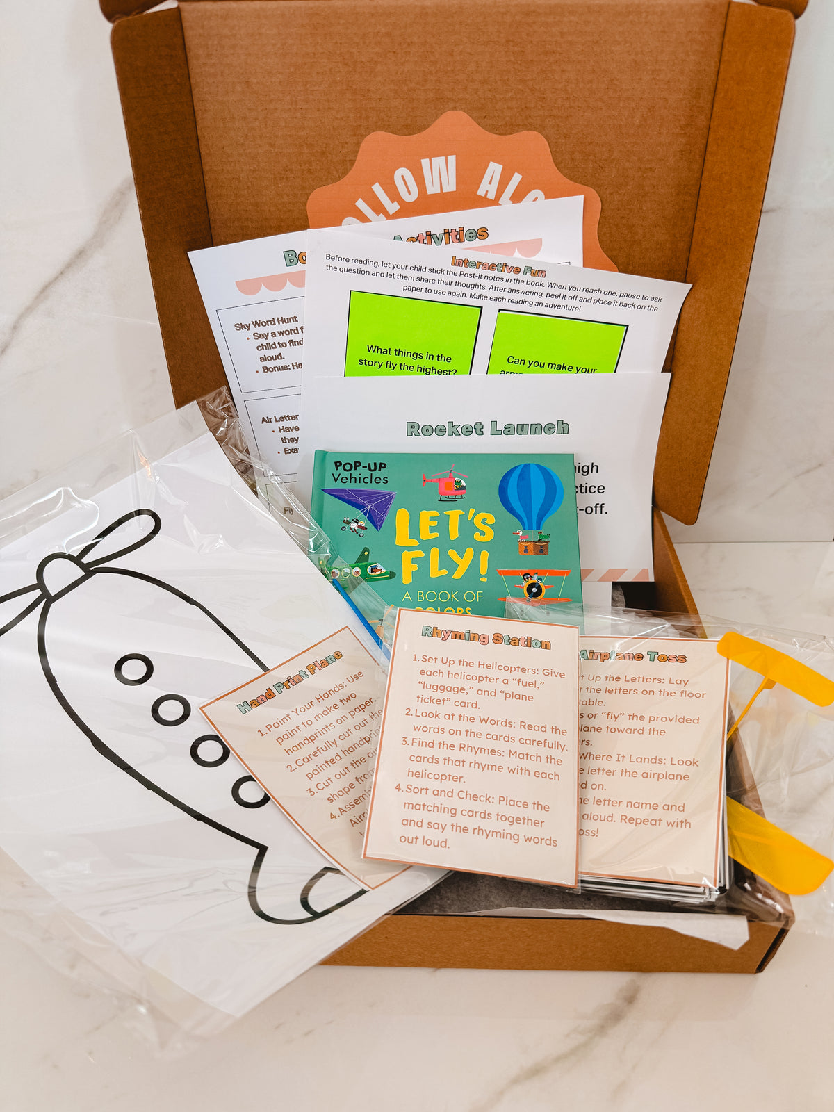 Educational children's items including a book and cards in an open cardboard box.