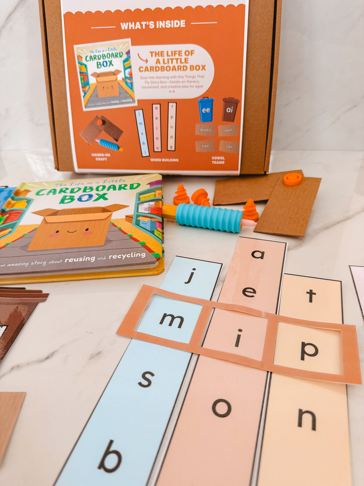 Educational materials including a cardboard box, alphabet cards, and a book on a marble surface.