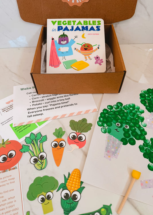 Children's book titled 'Vegetables in Pajamas' in a box with educational materials on a light surface.